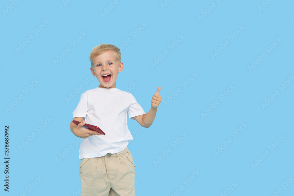 Cute smilling child boy with smartphone on blue background. Advertising of educational applications on a mobile phone for children. Funny face. Cute smilling child boy with smartphone on blue background. Advertising of educational applications on a mobile phone for children. Funny face.