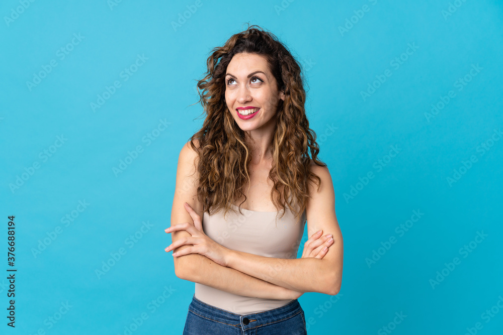 Fototapeta premium Young caucasian woman isolated on blue background looking up while smiling