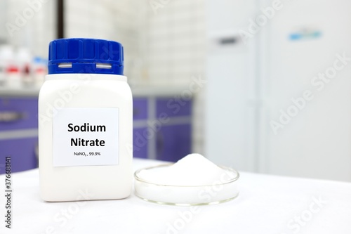 Selective focus of a bottle of sodium nitrate preservative compound beside a petri dish with white crystalline powder substance. White laboratory background with copy space. photo