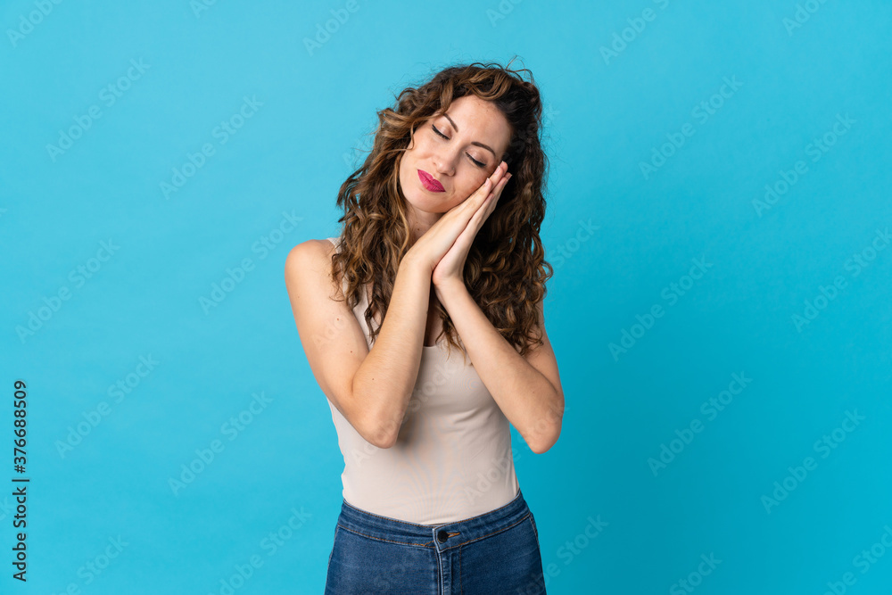 Young caucasian woman isolated on blue background making sleep gesture in dorable expression