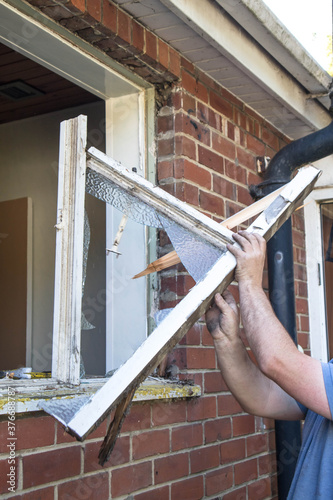 Workman removing old wooden window frame from a brick wall during home renovation