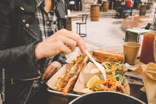 A woman s hand takes the ready-to-eat shrimp. Sea food in paper boxes on the table. Street food