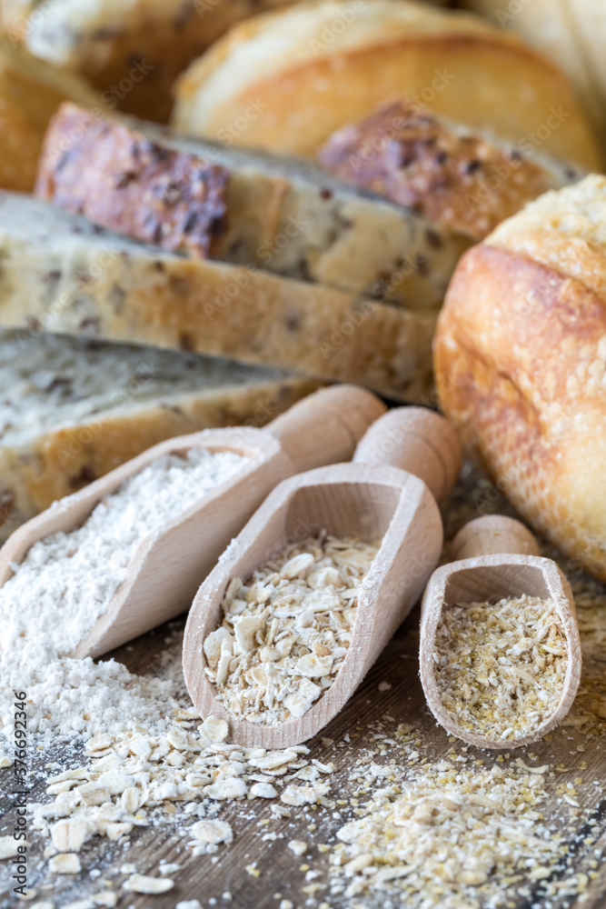 Close up of wooden scoops filled with flour, oats and oat bran and surrounded by bread.