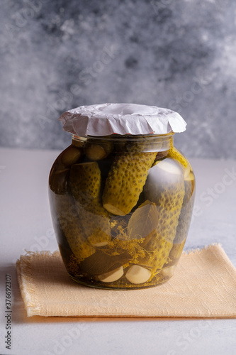 Preserved Canned cucumbers in a glass jar stands on a napkin on the table.