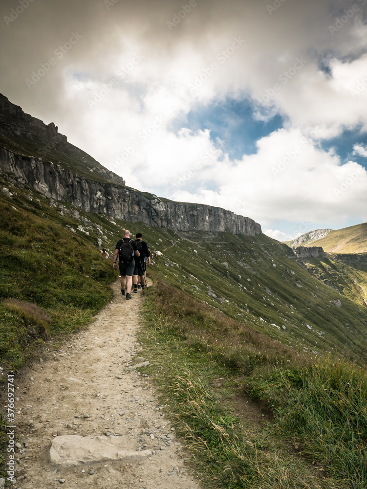 Hikers on the trail in the Bucegi Mountains against a dramatic sky.