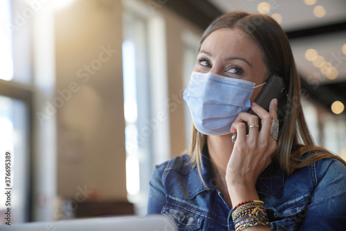 Young woman sitting at coffee shop and working on laptop with face mask