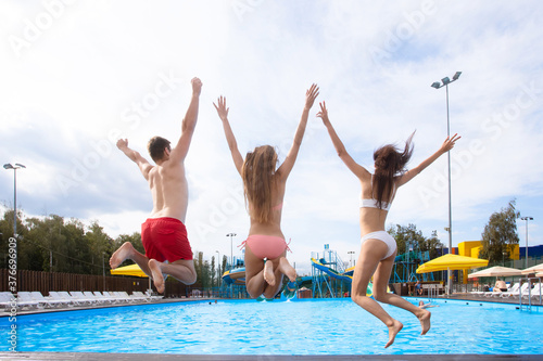 Group of young happy people jumping into swimming pool together. Summer party at the city pool. Friends spending their summer holidays and vacation. Hot sunny day. ..