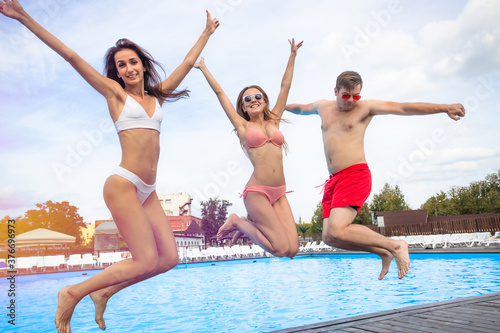 Group of young happy people jumping into swimming pool together. Summer party at the city pool. Friends spending their summer holidays and vacation. Hot sunny day. ..