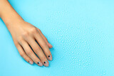 Womans hands with nude nail design over blue background with water drops