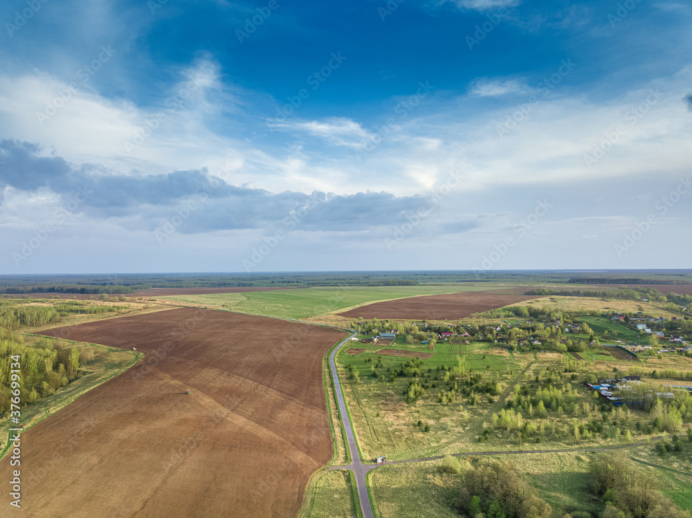 Aerial  view of the agricultural landscape with plowed fields, road and farm houses under bright blue sky with clouds. Summer day.