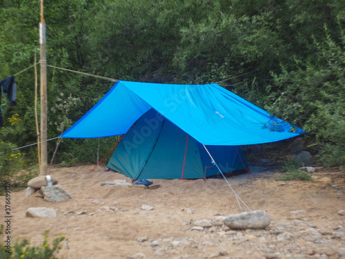 green tourist tent under a blue awning in the forest on a hike