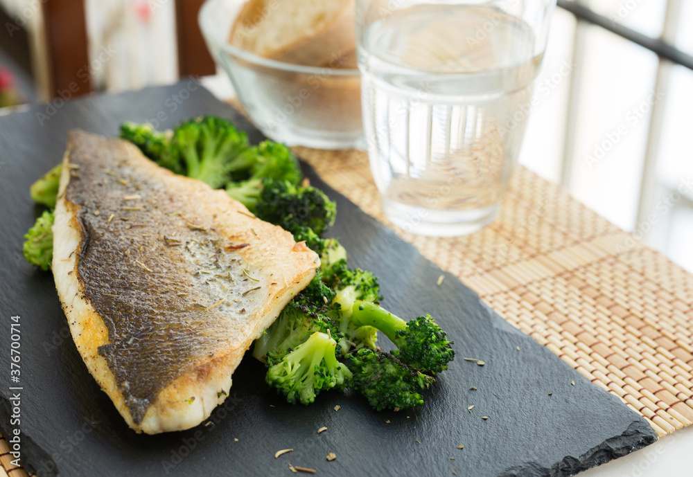 fried fillet of sea bass with garnish of broccoli on black warm stone plate fried fillet of sea bass with garnish of broccoli on black warm stone plate