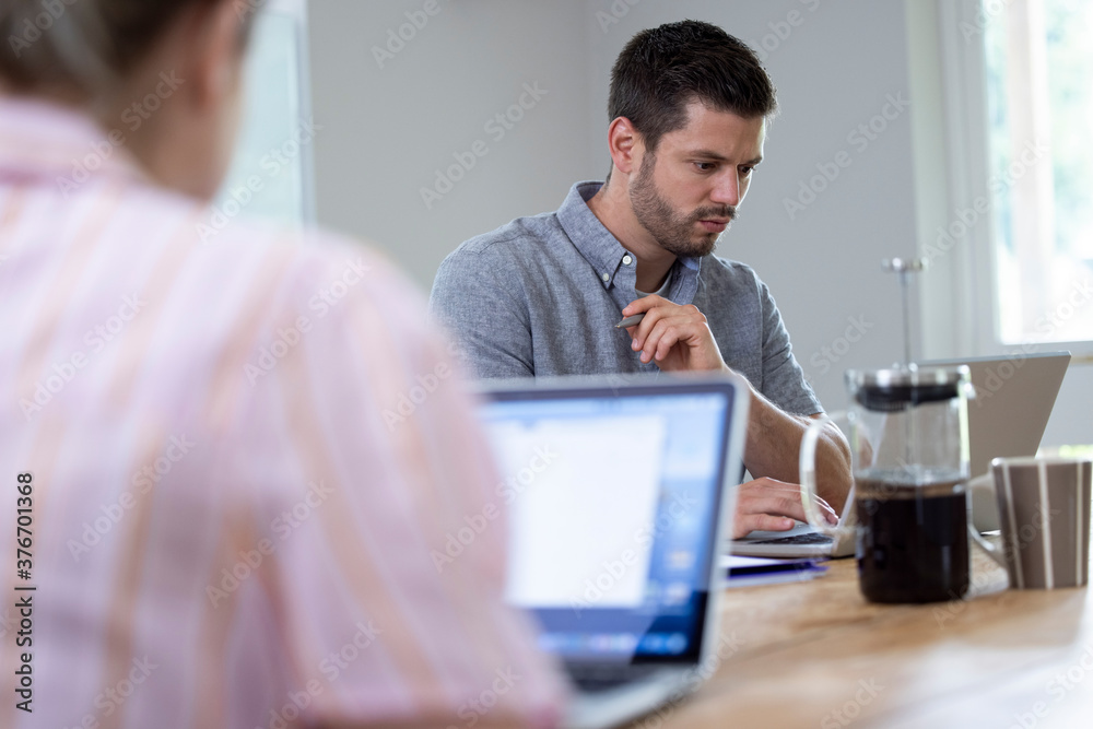Business Couple Working From Home Sitting At Table During Pandemic Lockdown