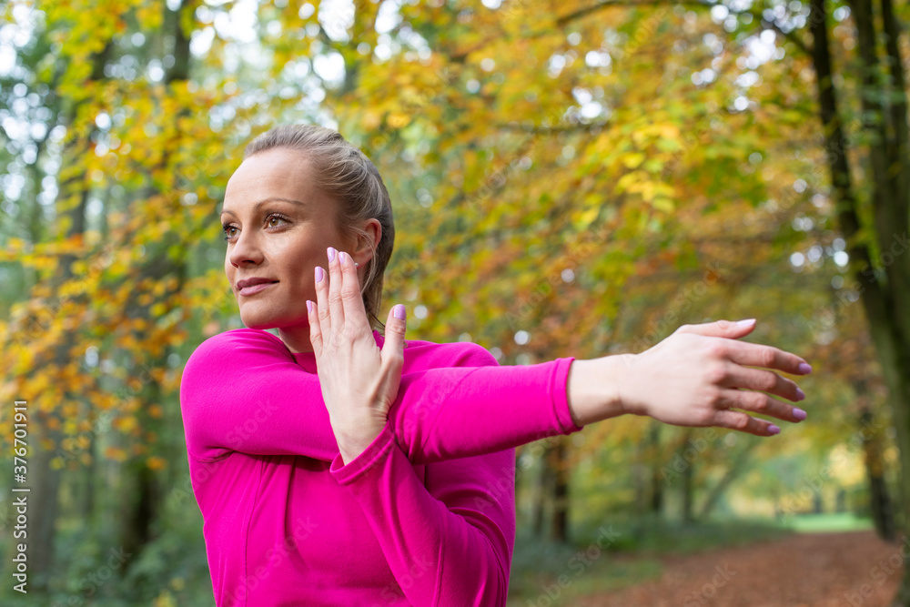 Side View Of Woman On Early Morning Autumn Run Through Woodland Stretching After Exercise