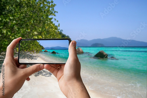 Fototapeta Naklejka Na Ścianę i Meble -  Man holding phone and taking picture of tropical beach with white sand and turquoise ocean. Vacation in tropical countries.