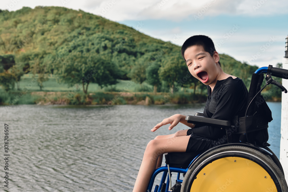 Disabled child on wheelchair is smiling, playing and exercise in the outdoor city park like other people,Lifestyle of special child,Life in the education age of children,Happy disability kid concept.