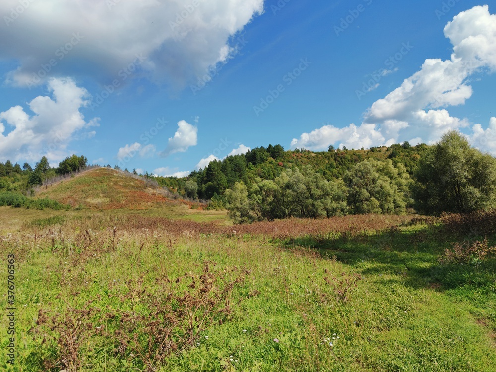 high hills among a green field against a blue sky with clouds on a sunny day high hills among a green field against a blue sky with clouds on a sunny day