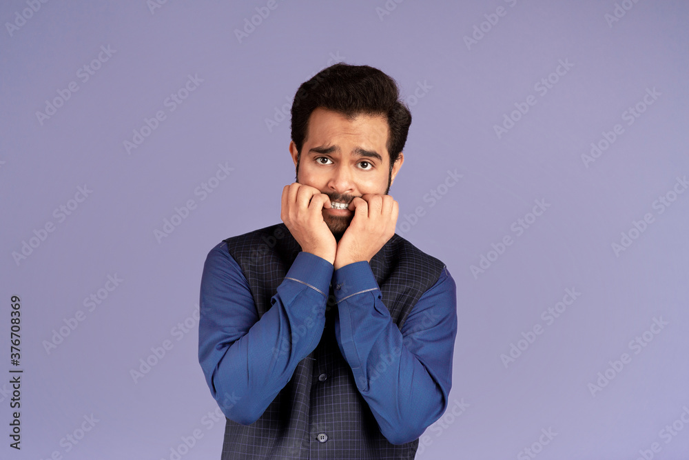 Terrified Indian man biting his nails in panic over lilac background Terrified Indian man biting his nails in panic over lilac background