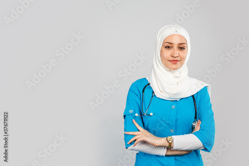 beautiful modern muslim doctor or nurse in hijab on a gray background. blue uniform.