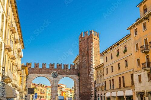 Fototapeta Naklejka Na Ścianę i Meble -  Portoni della Bra gate with merlons and clock, old Roman city double brick gate and medieval tower building in Verona historical centre, blue clear sky background, Veneto Region, Northern Italy