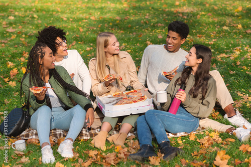 Carefree hipsters enjoying pizza, having picnic in forest