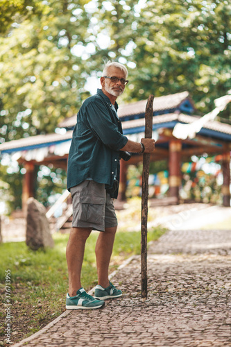 An old man with a stick and a backache is walking in the park. Hike in the 60s. © Andrii Zastrozhnov