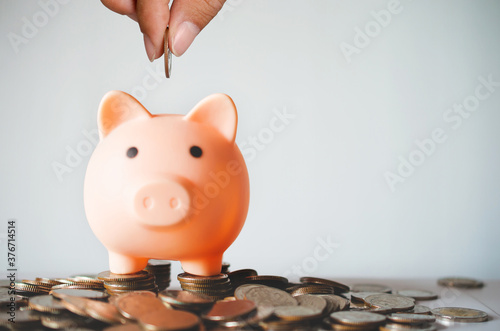 money saving concept. business hand putting golden coin in to piggy bank with stack coins on table white background for save and investment. financial and banking.