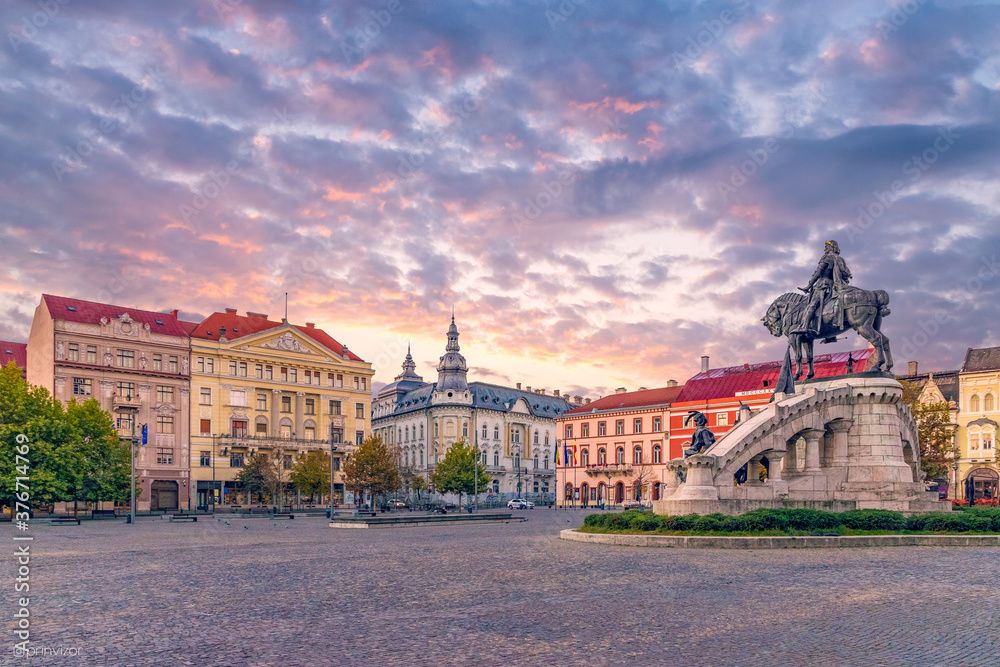 Cluj-Napoca city center. View from the Unirii Square to the Rhedey Palace, Matthias Corvinus Monument and New York Hotel at sunset on a beautiful day - obrazy, fototapety, plakaty 