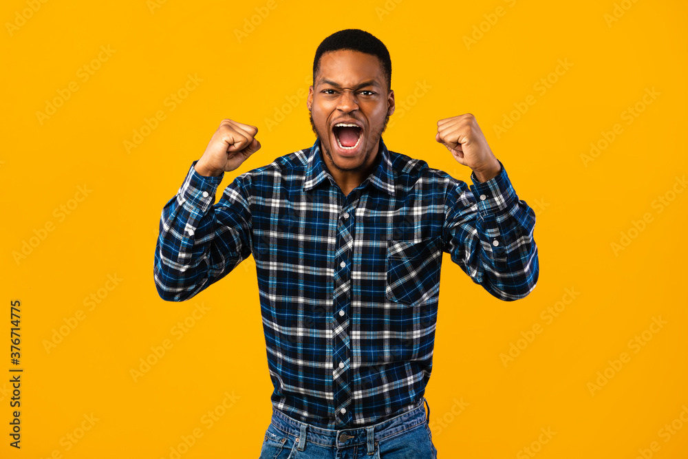 Naklejka premium Emotional African Man Shouting Loudly Shaking Fists Over Yellow Background
