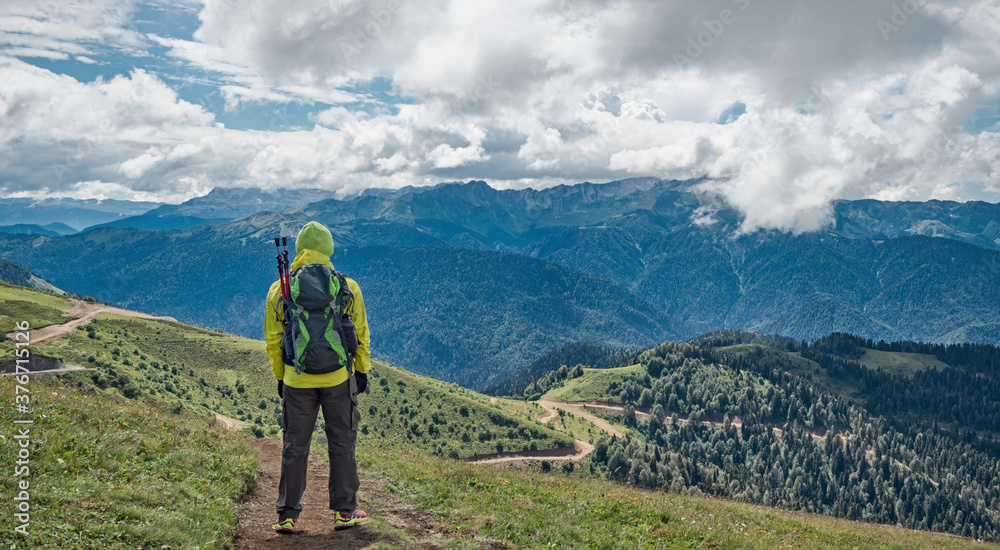 Naklejka premium Tourist with backpack at panoramic mountains and south slopes background in Rosa Khutor resort (Sochi, Russia)