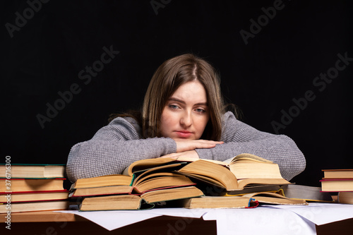 a young woman student sits behind a stoma with books with a sad look. exam preparation. difficulties of distance learning.