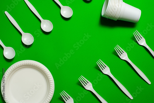 organic fork, spoon, plate and glasses of cornstarch on a green background. isolate. place for text. biodegradable tableware. ecologicaly clean. modern replacement for plastic. photo