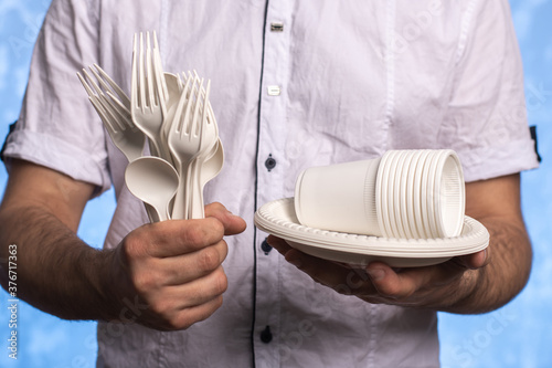 biodegradable cornstarch forks, spoons, plates and glasses in male hands. close-up. eco friendly concept. disposable cutlery photo