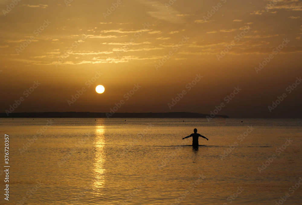 Minimalist silhouette composition of man standing in the sea during the sunrise or sunset