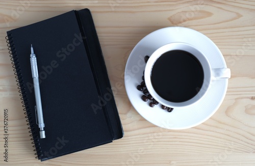 cup of coffee with beans and black notebook for copy space on wooden table background 