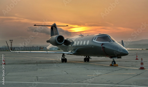 Front view of gray business airplane with two jet engines. Attractive orange cloudy sunset sky over the airport. Modern technology in fast transportation, business travel and tourism, aviation concept