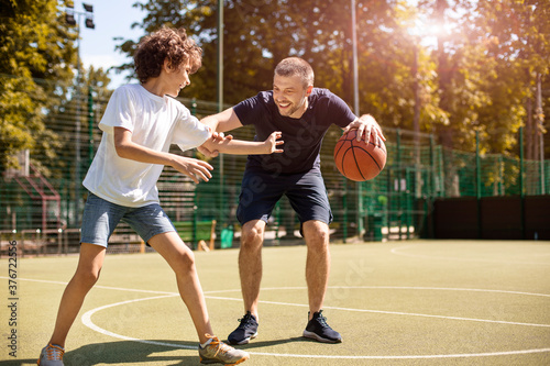 Mature man teaching boy how to play basketball