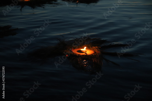 a burning candle in a wreath floats on the water at night