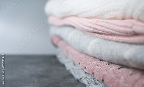 a pile of knitted sweaters in grey and pink colors. winter season clothes. selective focus. textured fabrics background. copy space for text or advertising. shallow depth of field.