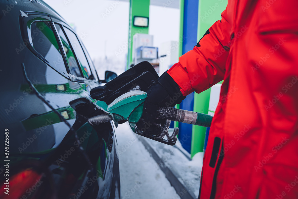Fototapeta premium Cropped image of male hand holding gas station pistol for refill for automobile in winter, gas station stop with oil pentor and fuels on refuel diesel