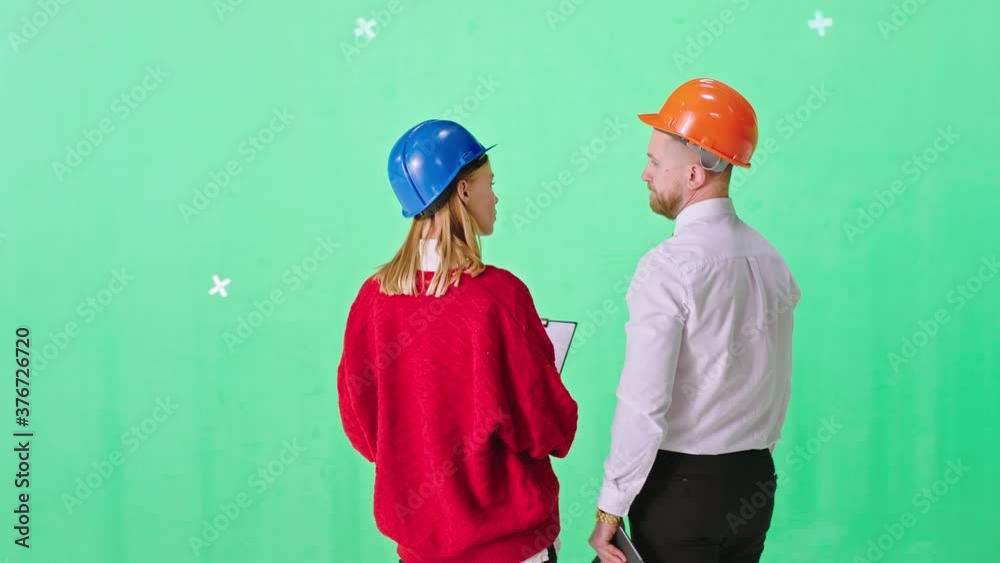 Young businessman and a lady engineer in a green background studio with a safety helmets analyzing the plan of construction site while holding a digital tablet. Shot on ARRI Alexa Young businessman and a lady engineer in a green background studio with a safety helmets analyzing the plan of construction site while holding a digital tablet. Shot on ARRI Alexa