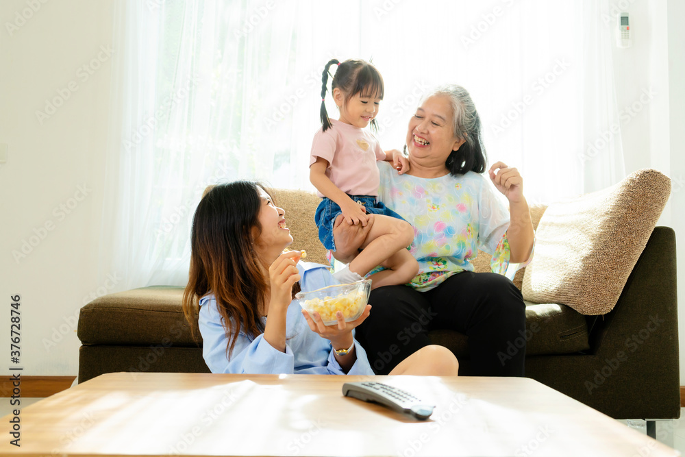 Three age ranges, Asian niece and grandma enjoying watching movies and eating popcorn in the living room in the house Three age ranges, Asian niece and grandma enjoying watching movies and eating popcorn in the living room in the house
