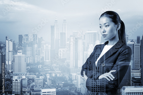 Prosperous Asian businesswoman in suit in crossed arms pose. Kuala Lumpur cityscape. The concept of woman in business. KL skyscrapers. Double exposure. photo