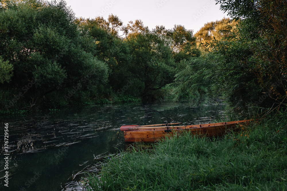 Obraz premium Calm water flow, morning fog and wooden boat. Summer or autumn sunrise over the river. Natural beauty of pristine nature. Water protection zone. Beautiful landscape banner. Card