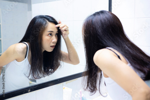 Asian women are exploring their faces due to acne. looks in the mirror and crushes pimple. Problem skin during menstruation. Acne and hyperandrogenism due to hormonal disorders.