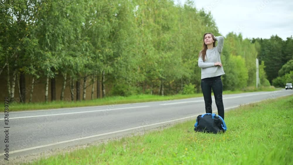 Young pregnant woman waiting for transport on the side of the road with a travel bag. Woman waiting for a bus or a ride outside the city Young pregnant woman waiting for transport on the side of the road with a travel bag. Woman waiting for a bus or a ride outside the city