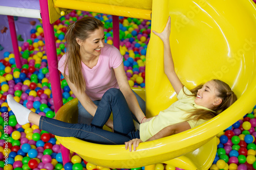 Mother and her daughter having good time on slide at kids playground, indoors