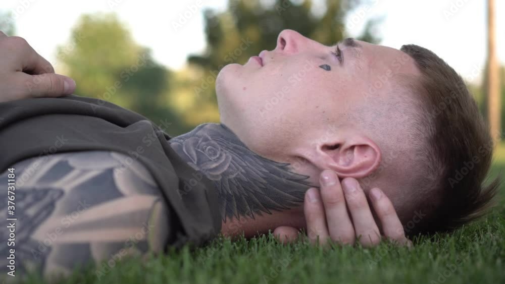 A young man with tattoos lies on the green grass, thinks and dreams A young man with tattoos lies on the green grass, thinks and dreams