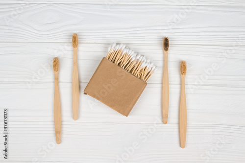 Cotton buds in kraft paper box and natural bamboo toothbrushes on white wooden background - zero waste bathroom essentials. Sustainable lifestyle concept. Mockup