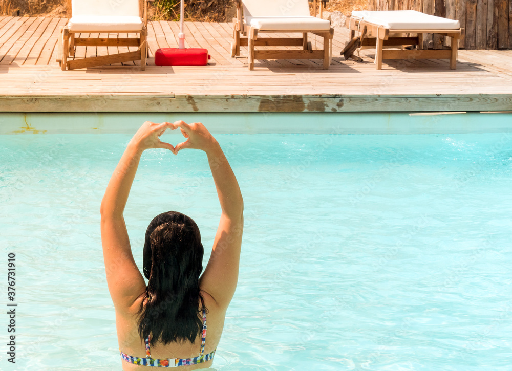 Young woman showing a heart symbol with hands at pool.